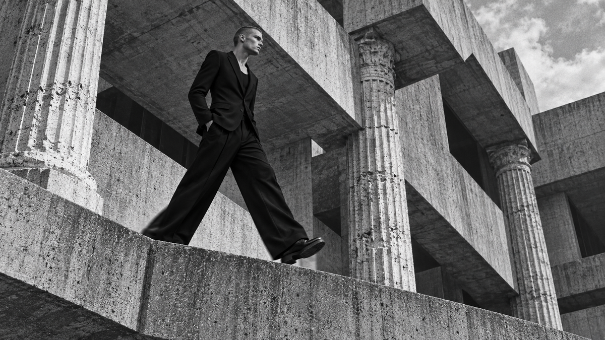 Male model in wide black tailoring moving through Roman and brutalist architecture