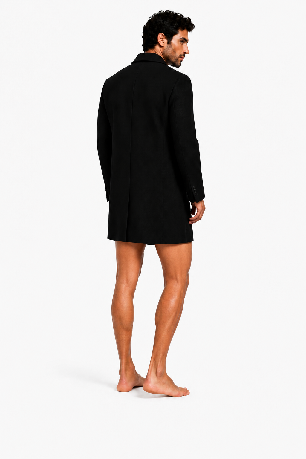 Male model wearing DOUBLE-BREASTED OVERCOAT 000 with very short black lycra shorts and bare feet — rear three-quarter view